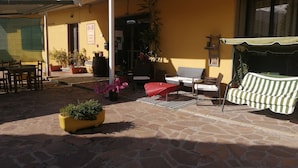 An outdoor patio area with stone flooring, a yellow building, a covered seating area, and potted plants. - Residence La Mezzaluna (Barga)