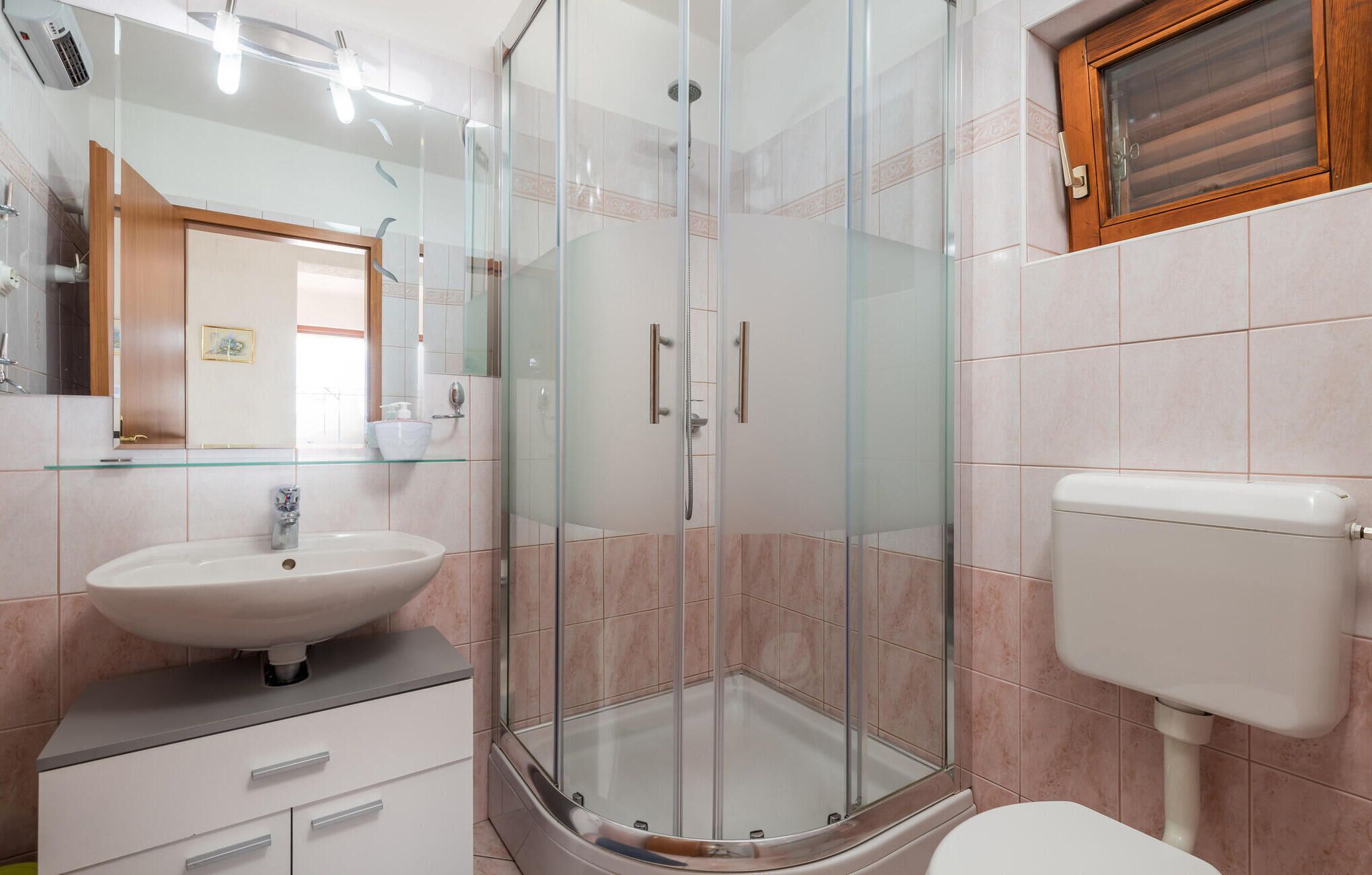 A modern bathroom with a glass-enclosed shower, a white sink, and a toilet.