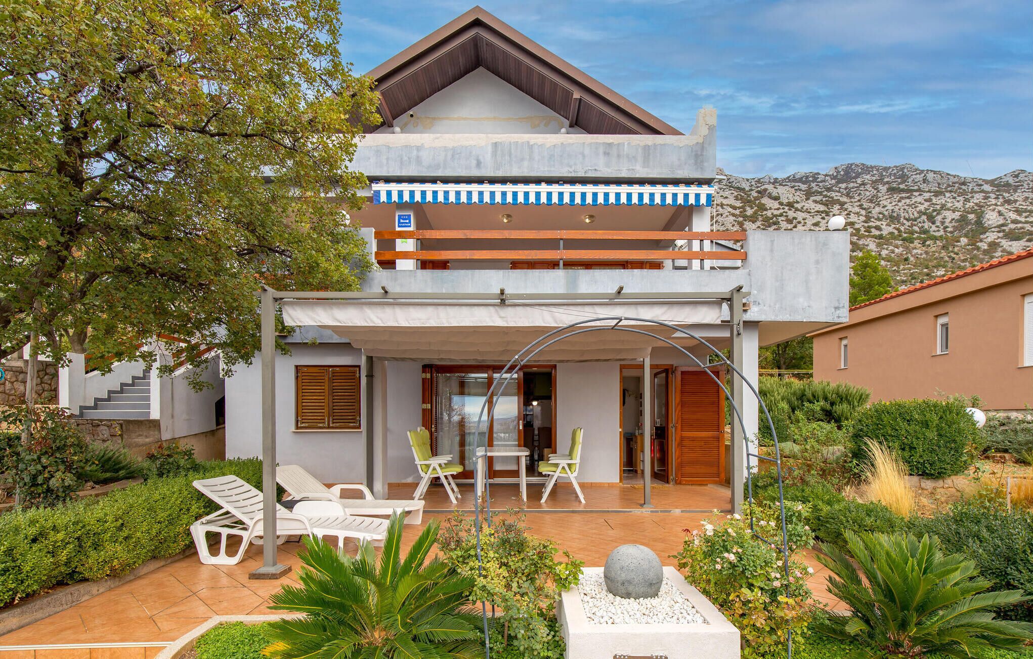 A modern two-story house with a balcony, outdoor seating area, and a garden.
