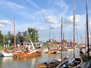 A marina with multiple boats docked, a clear sky, and a few people around.