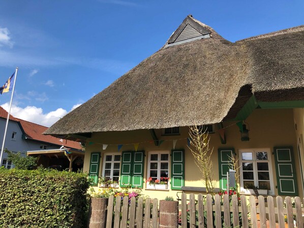Un bâtiment traditionnel avec un toit de chaume, des volets verts et une clôture en bois.