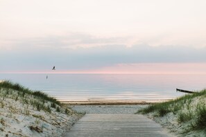 Une promenade en bois qui mène à une plage bordée de dunes de chaque côté.