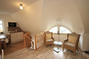 A loft-style room with a dining area, two wicker chairs, a small table, a TV, and a staircase.