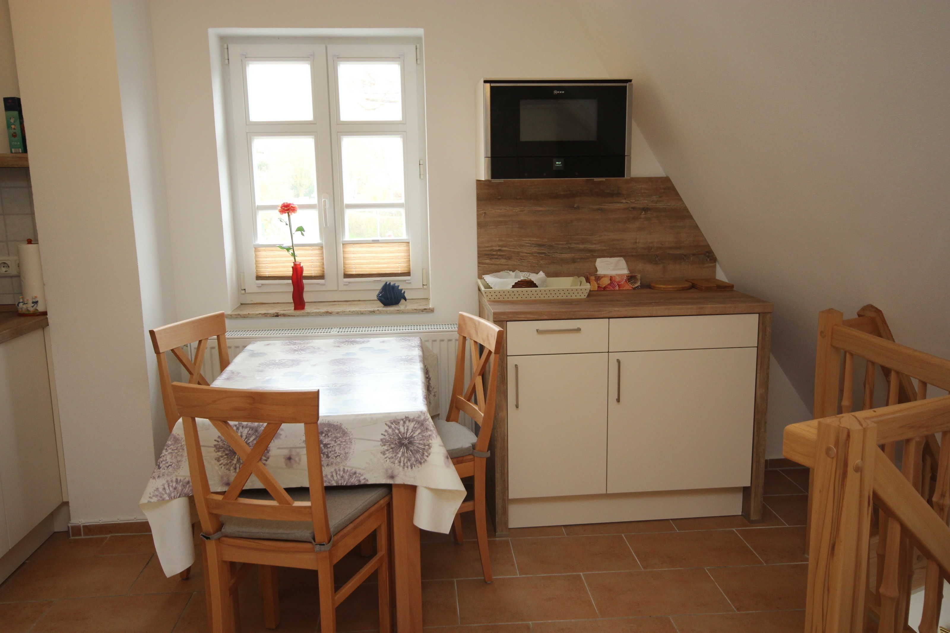A small kitchen with a dining table, chairs, a window with blinds, a TV, and a wooden cabinet.