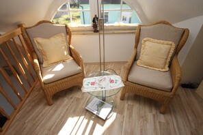 Two wicker chairs with cushions, a glass table with a book, and a window with a view of greenery. - In the thatched-roof house, Germany (Wustrow)