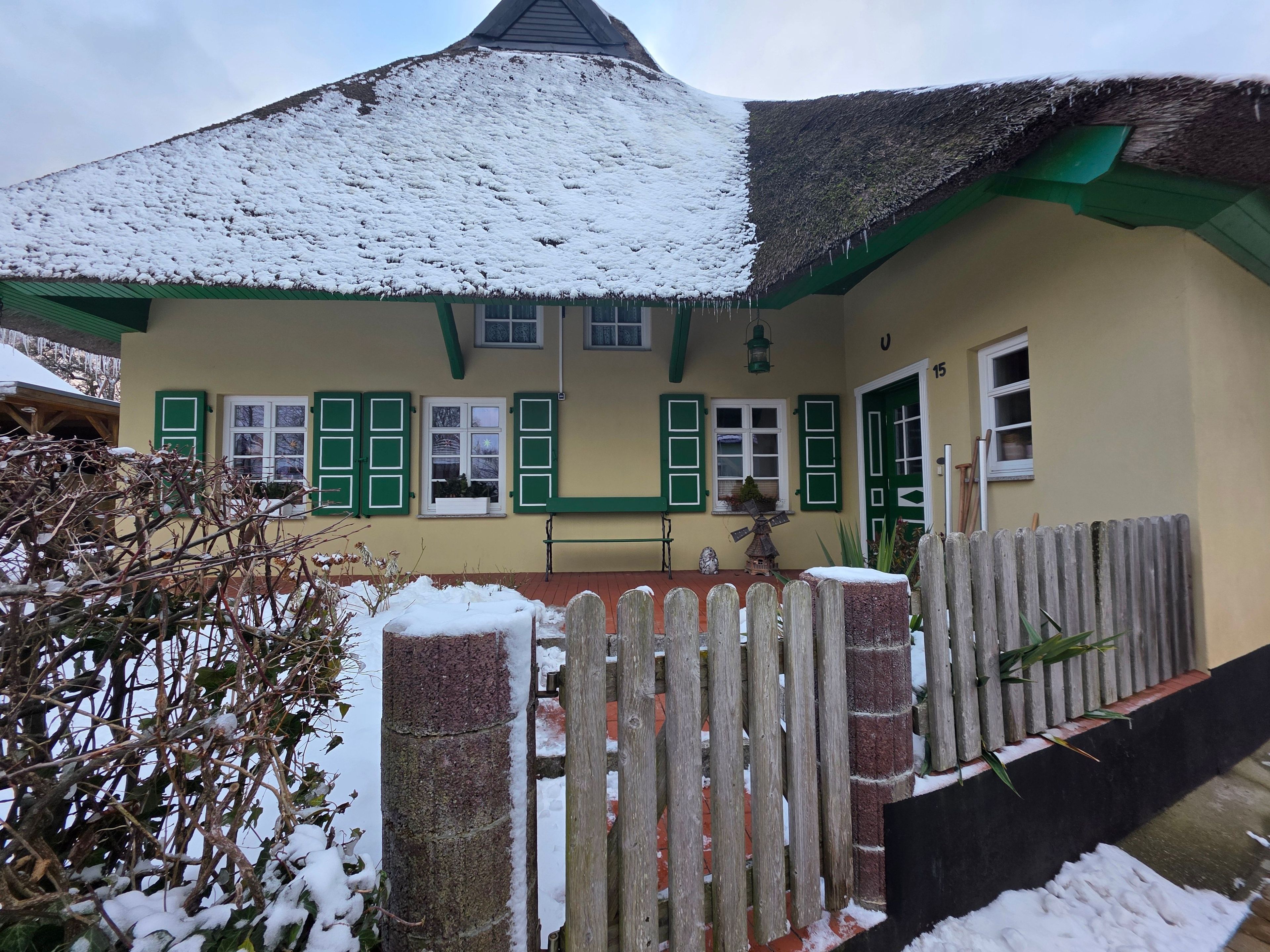 A house with a snow-covered roof, green shutters, and a wooden fence.