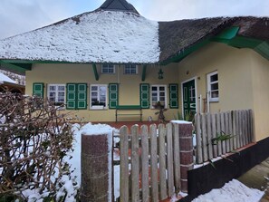 A house with a snow-covered roof, green shutters, and a wooden fence.