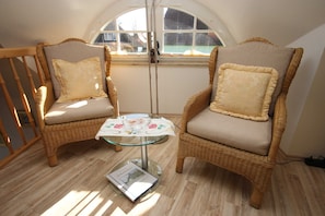 Two wicker chairs with cushions, a glass table with a decorative cloth, and a window with a view of a house.