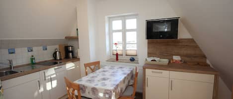 A small kitchen with a dining table, chairs, a TV mounted on the wall, and a window.
