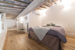 A bedroom with a wooden ceiling, a bed with a purple bedspread, a small bedside table, and a radiator.