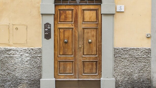 Une porte à deux battants en bois, avec une poignée en métal, une petite plaque et le chiffre « 5 » peint sur le mur.