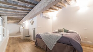 Une chambre avec un plafond en bois, un lit recouvert d’une couverture violette, une petite table de chevet et un radiateur.
