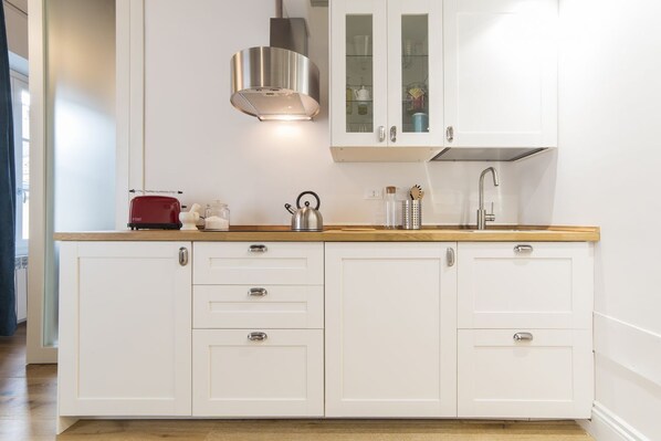 A kitchen with white cabinets, a stainless steel range hood, a wooden countertop, and a red toaster.