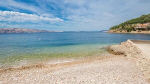 A coastal scene with clear water, pebbly beach, and distant rocky cliffs. - Beach front apartment in Starigrad with WiFi (Starigrad)