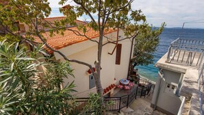 A coastal house with a tiled roof, a balcony with outdoor seating, and a view of the sea. - Beach front apartment in Starigrad with WiFi (Starigrad)