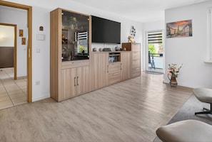 A modern kitchen with wooden cabinets, a flat-screen TV, and a dining area with a chair. - FeWo Galliet 1: 87sqm, 2 BR, balcony, quiet & close to trade fair (NRW)
