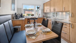 A modern kitchen with wooden cabinets, a dining table set for four, and a view of the outside. - FeWo Galliet 1: 87sqm, 2 BR, balcony, quiet & close to trade fair (NRW)