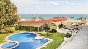 A pool with a view of the ocean, a building with a red roof, and a palm tree.