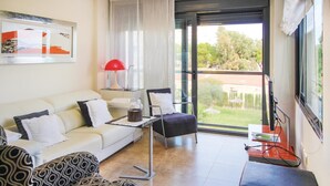 A modern living room with a sofa, a patterned armchair, a small table with a lamp, and a view of the outdoors through a glass door.