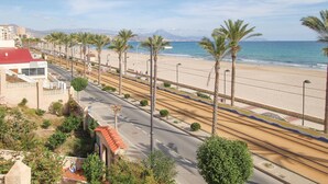 A coastal road with palm trees, a beach, and a mountain in the background.
