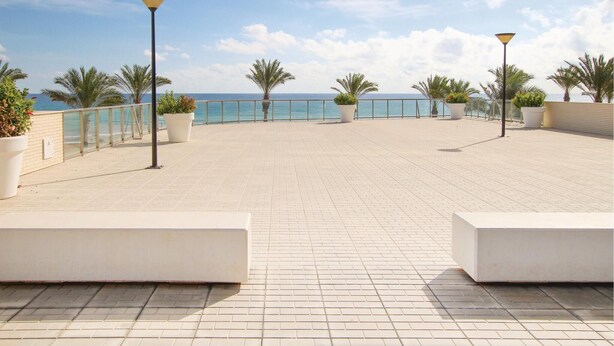 A spacious outdoor terrace with a tiled floor, potted plants, and a railing overlooking a body of water.