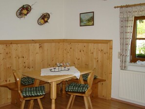 Une table de salle à manger en bois, accompagnée de quatre chaises, d’une nappe blanche et de coussins à carreaux.
