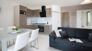 A modern kitchen with a built-in oven, a dining table with chairs, and a black leather sofa with a mirror. - Beautiful apartment in Rabac with WiFi (Rabac)