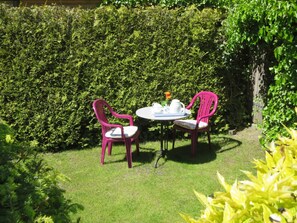 Ein Garten mit Tisch und zwei Stühlen, umgeben von viel Grün.