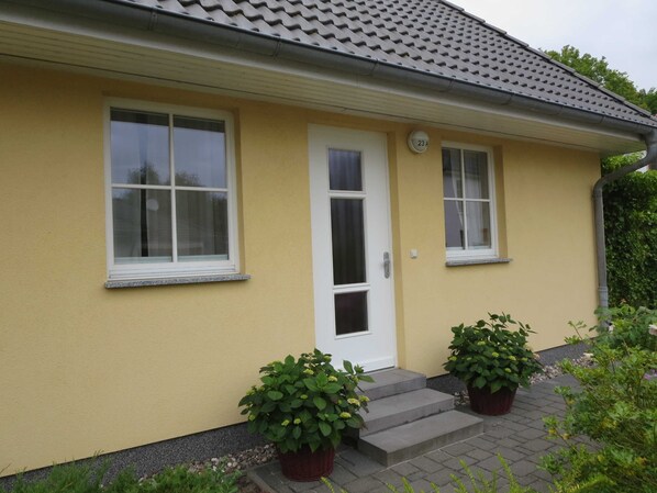Ein gelbes Gebäude mit einer weißen Tür, zwei Fenstern und einer kleinen Veranda mit Blumentöpfen.