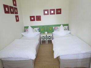 Une chambre avec deux lits simples, une petite table, deux chaises et un mur orné de six éléments décoratifs carrés.
