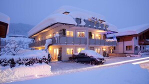 Un edificio a più piani con balconi, un paesaggio innevato e un'auto parcheggiata davanti.