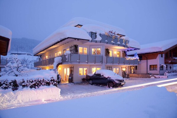 A multi-story building with balconies, snow-covered surroundings, and a car parked in front.