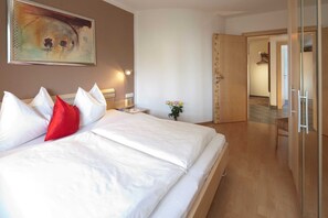 A hotel room with a large bed, a nightstand, a painting on the wall, and a door leading to another room. - Top 1 - 3 (1) - Apartment block Charisma (Fieberbrunn)