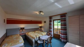 Une chambre d’hôtel avec deux lits, une petite table, une chaise, un bureau, une armoire et une fenêtre avec des rideaux.