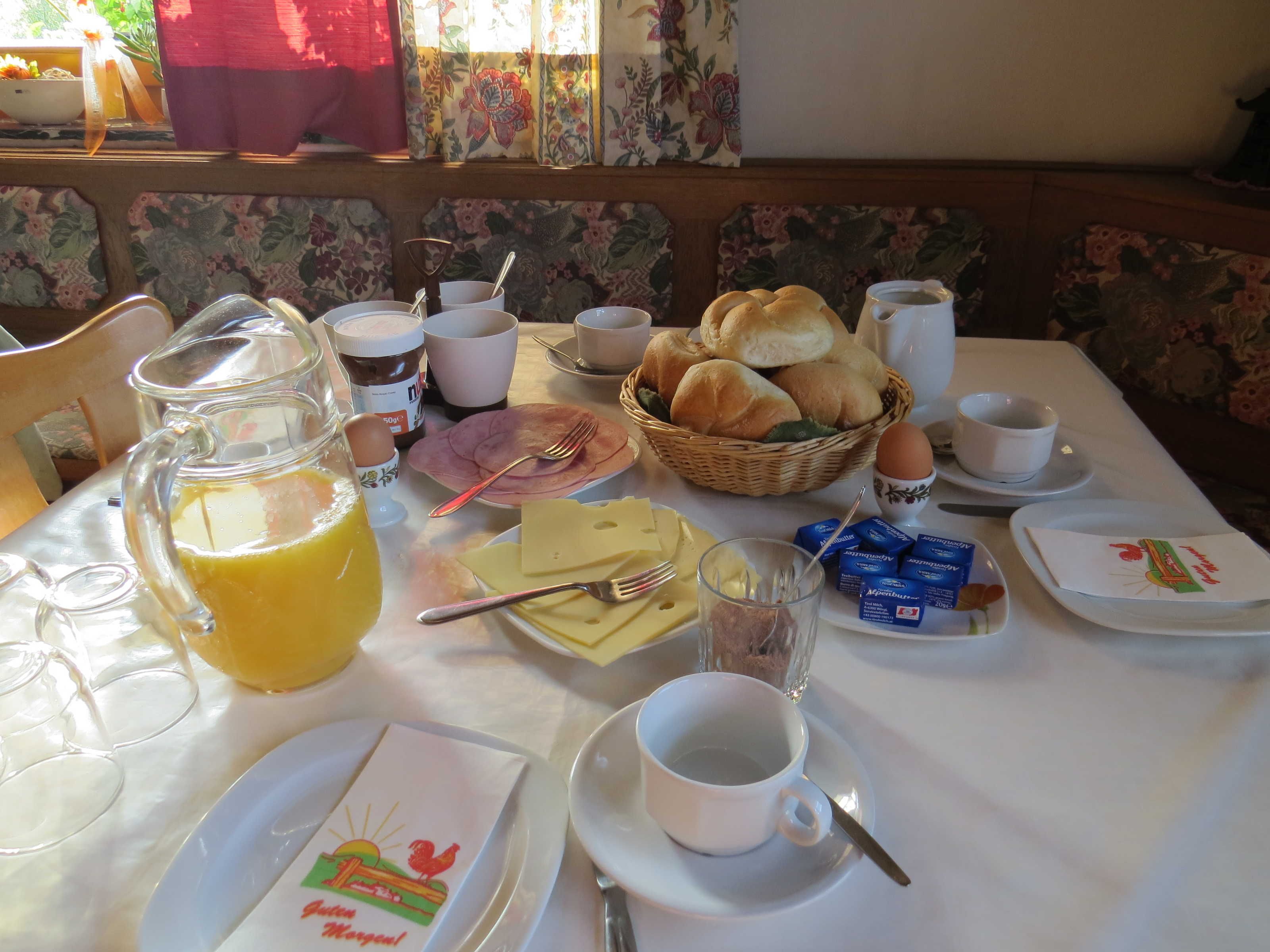 Ein Esstisch mit verschiedenen Speisen, einer Saftkanne und einer Kaffeetasse.