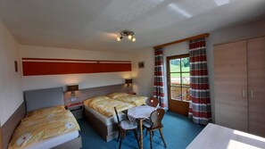 Una habitación con dos camas, una mesa y sillas, una lámpara en el techo y una puerta con cortinas.