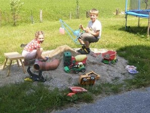 Deux enfants jouent avec des voitures miniatures et des jeux de construction dans un espace extérieur recouvert d’herbe.