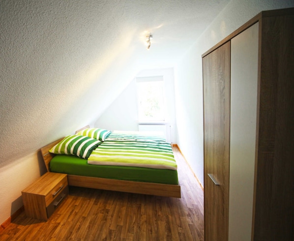 Una habitación con una cama, una mesita de noche de madera, un armario y una ventana.