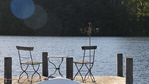 A wooden dock with two metal chairs and a table, overlooking a calm lake. - Duck's Nest - Thatched Aspen House (Grebin)