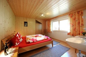 Ein Zimmer mit Holzwänden, einem Bett, einer Holzbank, einem Fenster mit Vorhängen und einem Waschbecken.
