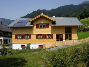 Ein zweistöckiges Holzhaus mit geneigtem Dach, Solaranlagen und einem Holzzaun.