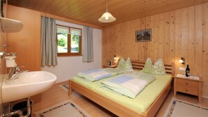 A wooden-paneled bedroom with a bed, bedside tables, a window with curtains, a sink, and a hanging light fixture. - Bischof Reingard - Apartment 2 1 (Schoppernau)