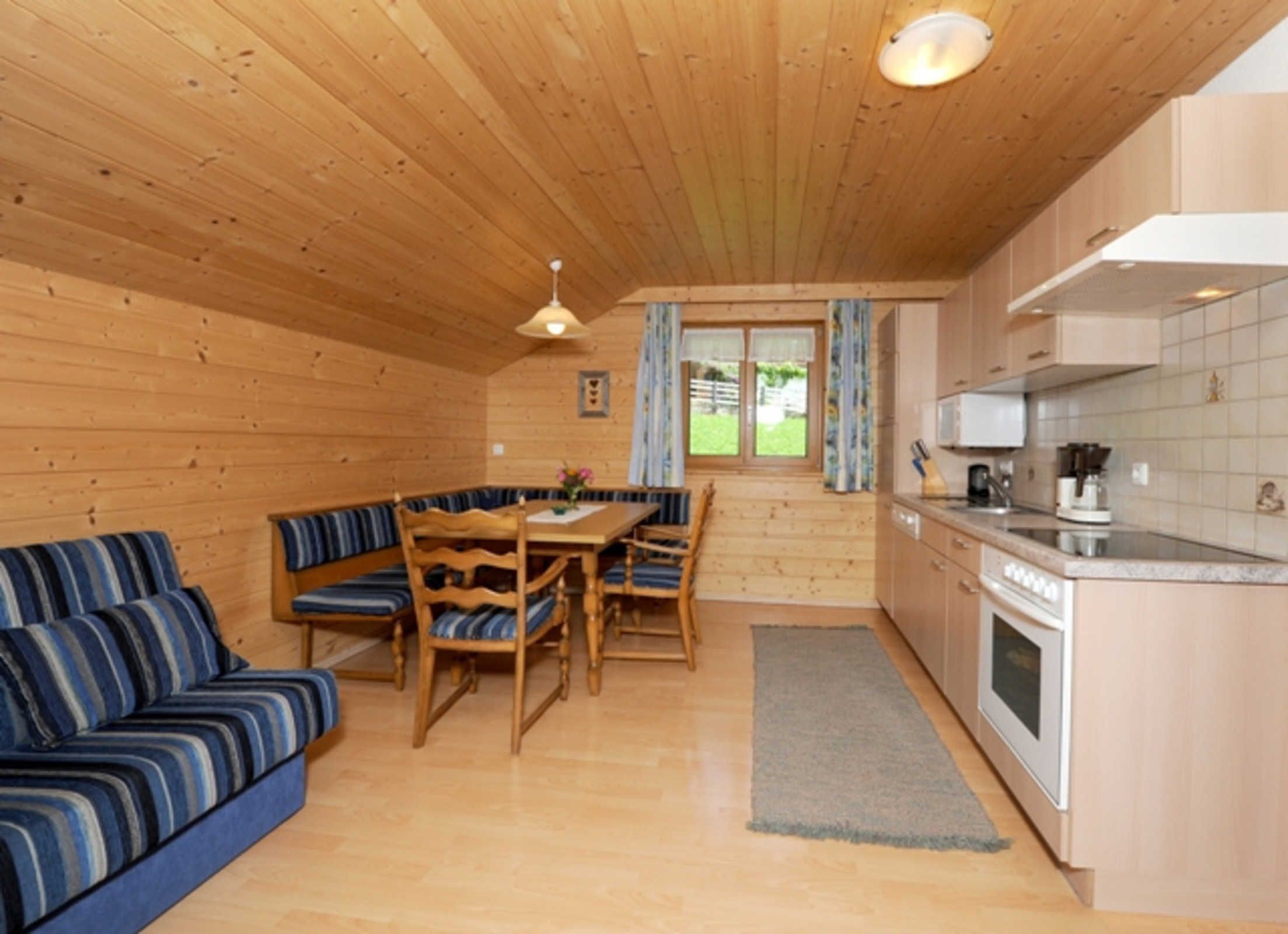 Ein Holzblockhaus-Interieur mit Essbereich, Sofa, Küche und Blick durch das Fenster.