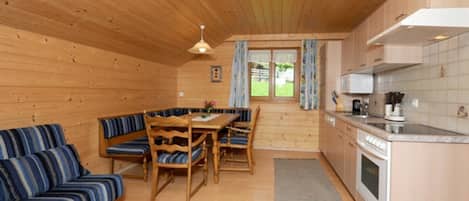 Interior de una cabaña de madera con comedor, sofá, cocina y vistas por la ventana.