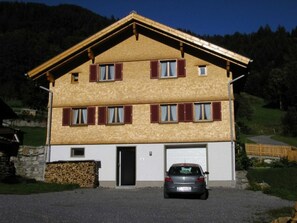 A two-story house with a garage, a car parked in front, and a stone wall at the base.