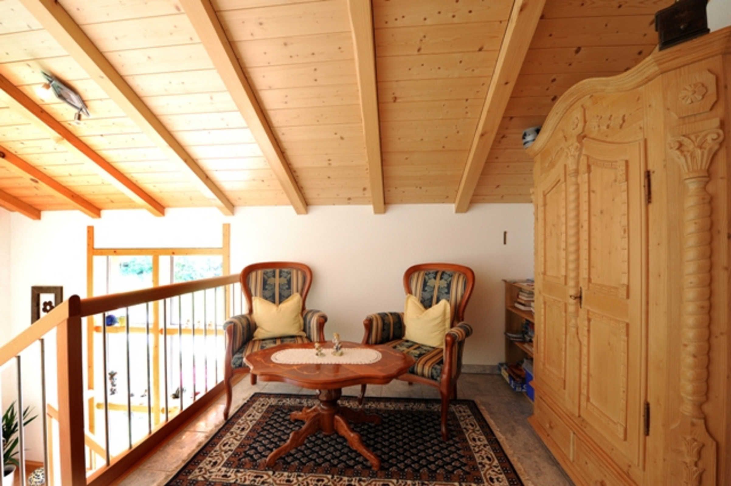 A wooden-floored room with two upholstered chairs, a round table, and a wooden cabinet.