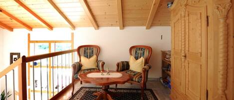 A wooden-floored room with two upholstered chairs, a round table, and a wooden cabinet.