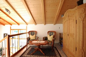 Une pièce au plancher de bois, avec deux fauteuils rembourrés, une table ronde et un buffet en bois.