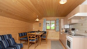 A wooden cabin interior with a dining area, sofa, kitchen, and a view through the window. - Bischof Reingard - Apartment 2 1 (Schoppernau)
