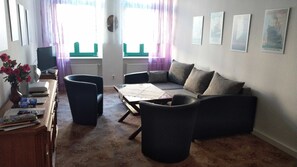 Uma sala de estar com um sofá, duas poltronas, uma mesa de centro, uma televisão e um vaso com flores.
